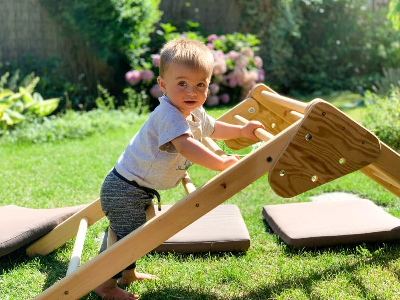Kleinkind klettert im Garten auf Montessori Kletterelement